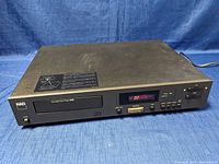 Front and top view of black NAD 5220 compact disc player sitting on blue fabric background, showing front-loading disc tray, control buttons, digital display, and power switch.