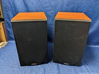 Front view of a pair of Paradigm Titan V4 bookshelf speakers with black fabric grilles attached, showing brand logos and wood veneer sides.