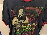 Front view of black Bob Marley T-shirt featuring colorful graphic of Bob Marley with guitar, on red trimmed collar and sleeves.