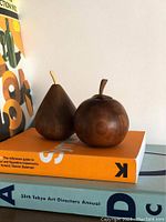 Two carved wooden fruit figures on top of books showing pear and tomato shape in dark brown wood with smooth finish.