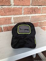 Front view of black Gongshow Big Shooter hat with camouflage pattern and neon yellow outlined shooter patch