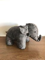 Grey faux leather elephant-shaped door stopper side view on wooden surface with visible textured faux leather and details.