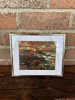 Front view of framed print showing the artwork depicting red maple leaves and a stream with rocks.