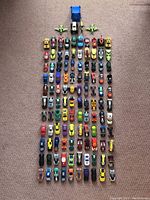 Top-down photo showing approximately 80 Hot Wheels toy cars arranged in neat rows on carpet. Cars show various designs with McDonald's logos and diverse colors.