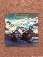 Front cover of the John Denver Rocky Mountain Christmas vinyl album showing snow-covered mountain village artwork with album title