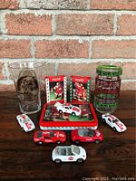 Lot includes six Coca-Cola diecast cars in red and white, two Coca-Cola themed drinking glasses, and holiday playing cards tin with two decks.