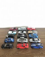 27 Maisto diecast toy vehicles displayed on wooden surface, including cars in various colors and styles, some with visible wear.