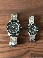 Two MazdaSpeed wristwatches side by side on a wooden surface showing faces and bracelets