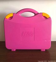 Front view of bright pink LEGO plastic carrying case with handle, embossed LEGO logo and yellow latch clips
