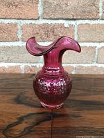 Front view of cranberry glass vase showing ruffled top and quilted textured bottom.