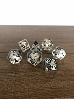 Clear polyhedral dice with black skulls inside and black numbering arranged on wooden surface.