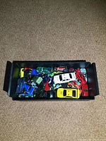 Top-down photo of a black plastic tray filled with approximately 20 diecast toy cars in various colors including green, white, red, yellow, blue, and black.