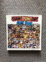Top view of the puzzle box showing the vibrant comic book collage artwork and the title Bam! Pow! Zap! Comic Book Puzzle.
