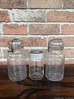 Front view of all three jars: two large Perfect Seal jars with wire clamp lids and one smaller GEM jar with twist top lid.