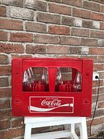 Front view of red Coca Cola plastic delivery crate with 8 bottles inside showing classic white Coca Cola logo.
