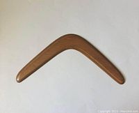 Full view of the vintage wooden boomerang showing its smooth curved shape, minor scratches present.