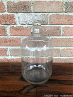 Full view of clear glass jug with handle and twist cap against brick background