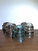 Front view of three vintage Dominion railway glass insulator caps shown side by side on wooden surface with shadows behind.