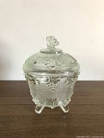 Front view of the vintage Jeanette Glass candy dish, showing grape and leaf design on lid and base, standing on three legs.