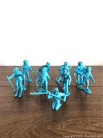 Front view of nine blue plastic Arctic explorer toy figures arranged on wooden surface, various standing and skiing poses