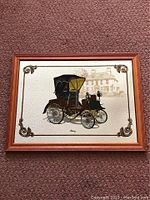 Full view of the framed mirror showing the painted vintage Mercedes Benz carriage image and wooden frame resting on carpet.