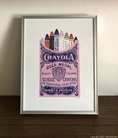 Full front view of the framed vintage style Crayola crayon box illustration print on a wood surface against a plain wall.
