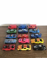 Photo showing 15 vintage diecast toy cars including red, blue, green, yellow, pink, and black race and sports cars, as well as vans.