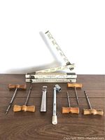 Photo showing folding rulers unfolded and several gimlets with wooden handles laid out, along with a pressure gauge and bottle opener.