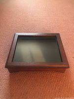 Closed wooden display case with glass lid resting on carpet.