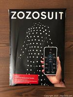 Front view of the packaging showing the ZOZOSUIT name, graphic of a black full-body suit with white dots, and smartphone app interface representing measurement system.
