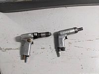 Two metal air drills with pistol grip laid side by side on a white surface showing their size and shape