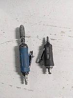 Two pneumatic air grinders, one black Porter-Cable and one blue Power Fist brand, placed side by side on a white surface showing the full length and mounted grinding bit on the Power Fist.