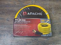 Photo showing Apache brand PVC air hose boxed and sealed, with product label visible indicating 3/8" x 50' and 300 PSI.