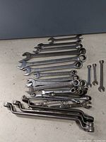 Array of wrenches laid out showing various sizes, mostly combination wrenches with open and box ends, and some open end only.