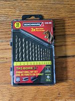 Front view of Benchmark 13-piece Cobalt Tri-Bore drill bit set in factory sealed plastic case showing 13 drill bits and packaging labels.
