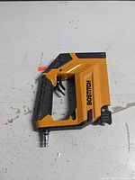 Front and side views of yellow and black pneumatic Bostitch crown air stapler with grip and air hose connector.