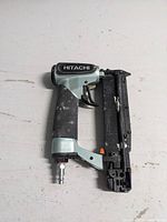Side view of Hitachi NP 35A pin nailer showing paint and scuff marks with Hitachi branding on the barrel, pin magazine attached and air hose connector at the base.