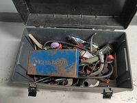 Opened plastic toolbox showing mixed contents including clamps, brushes, file, small tools and hardware scattered inside.