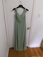 Full length front view of the sage green bridesmaid dress hanging on a door.
