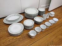 Full set arranged on wooden floor showing all major pieces in the Noritake Savannah 2031 53-piece fine china set with cups, plates, creamers, sugar bowl and bowls.