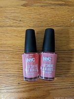 Two bottles of pink NYC nail polish with black caps on wooden surface.