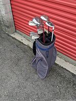 Wilson golf cart bag with the golf clubs inside, showing side pockets and full set standing upright next to a red garage door