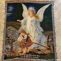 Woven throw blanket showing large angel with wings and two children on a bridge at night with text on bottom.