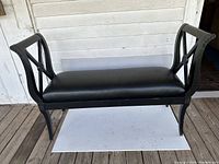 Front view of black wooden bedroom bench with black leatherette upholstered seat showing slight wear and use.