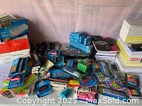 Photo showing a variety of school supplies including colored pencils, markers, pens, sharpeners, calculators, and paper packs spread on a table.