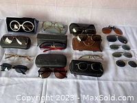 Full view of the sunglasses lot spread out on a cloth, showing the variety of styles and cases included