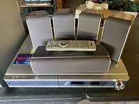 Home theater system components including 5 speakers, center channel speaker, main unit with remote on top.