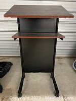 Front view of the mobile adjustable height stand up desk lectern podium with two dark wood shelves and black frame.
