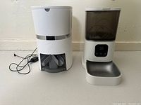 Photo of two automatic pet feeders placed side by side on the floor, showing overall size and design