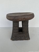Side view of the vintage hand-carved wooden stool, showing the detailed carvings on the two cylindrical supports and base.